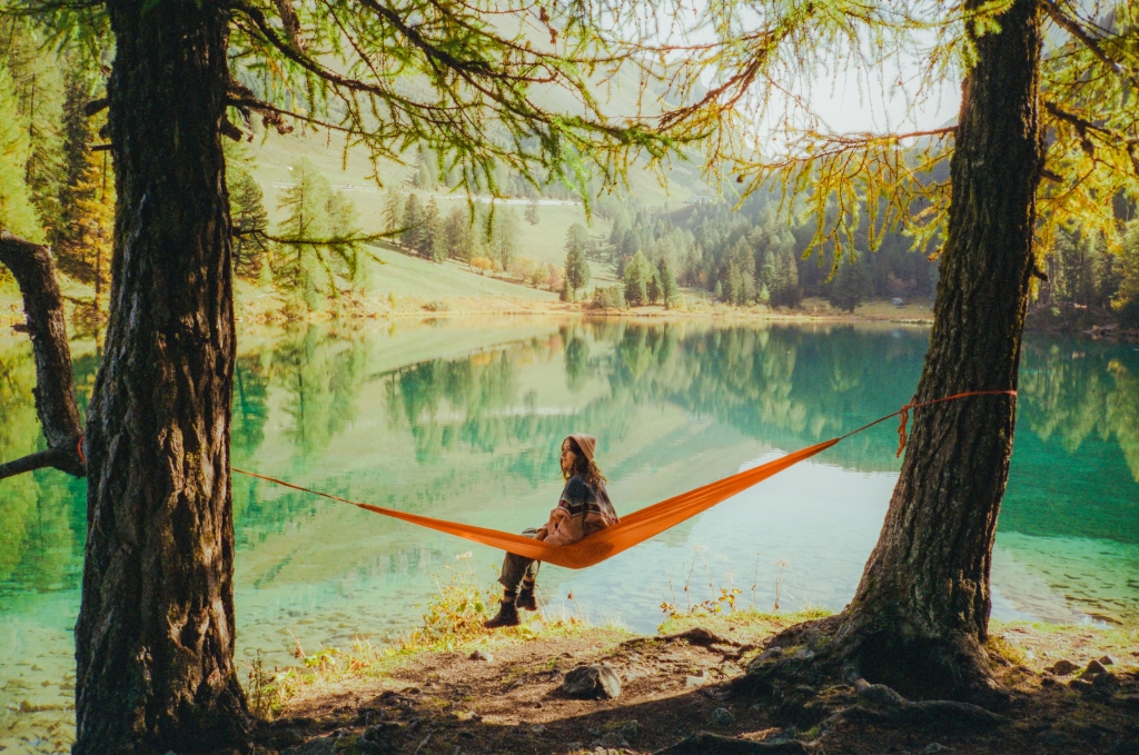 Young Caucasian woman resting in hammock on the background of the lake in Swiss Alps in autumn